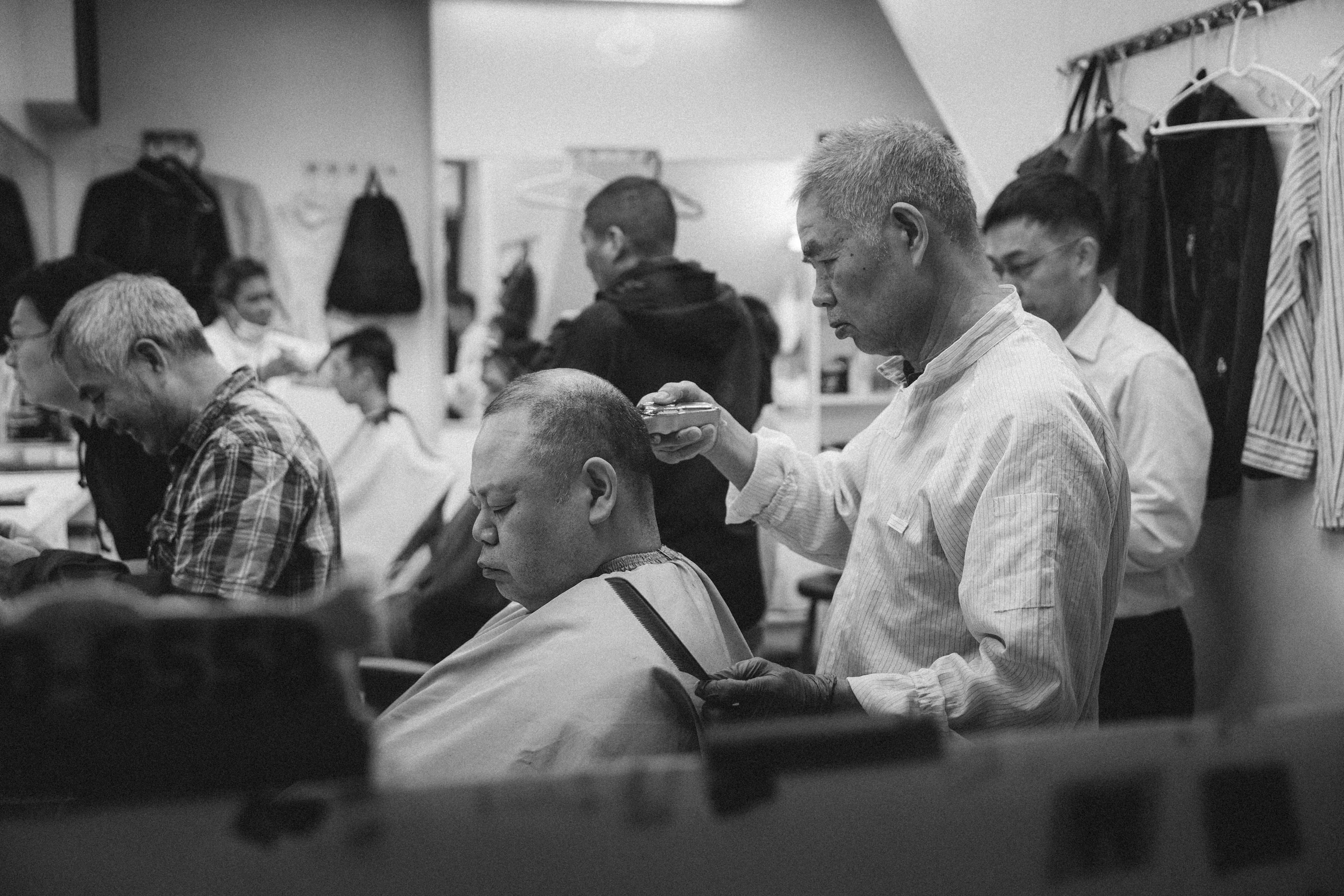 Barber cutting a customer's hair in a busy barbershop