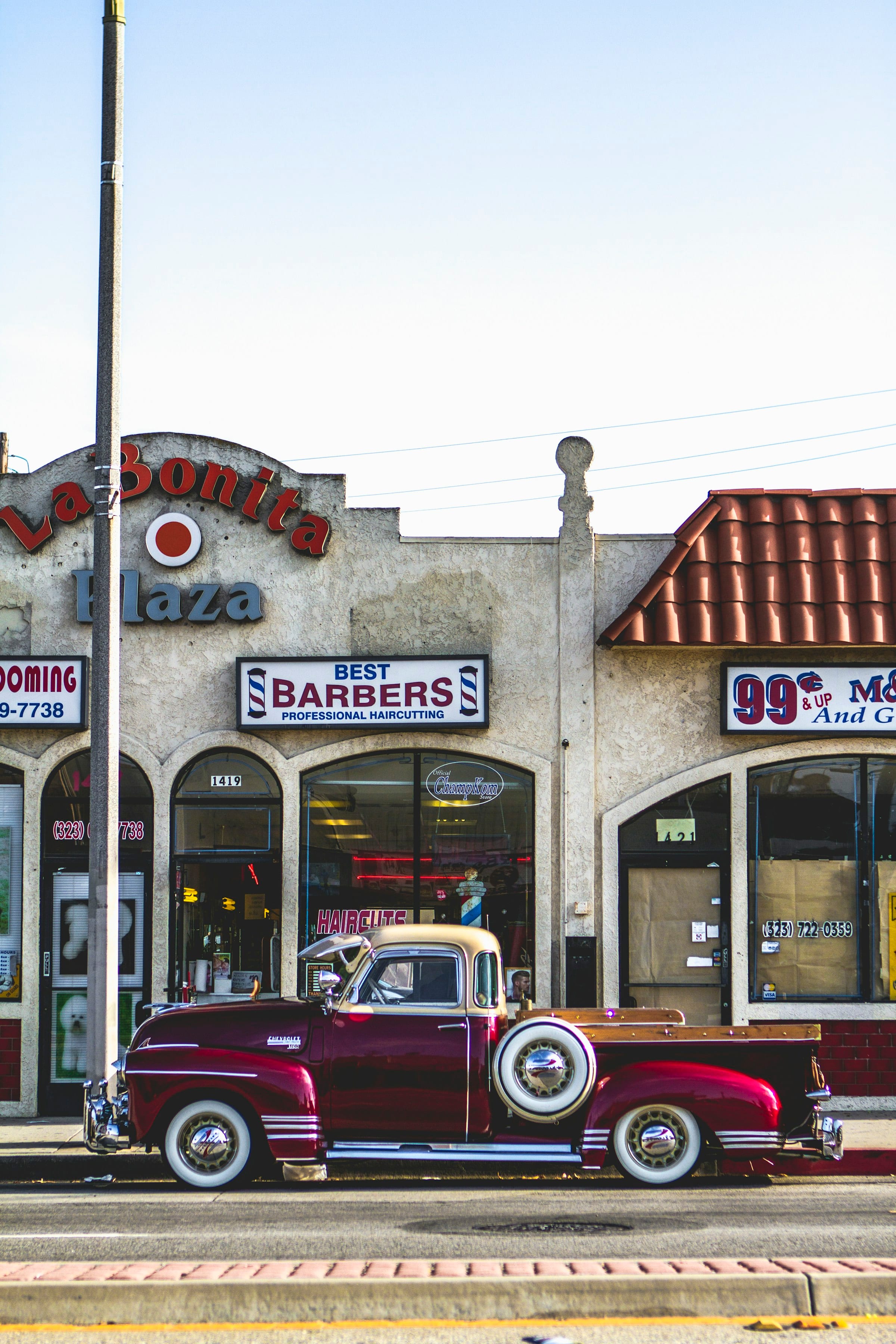 Sunny barbershop storefront with vintage signage and a red classic pickup outside