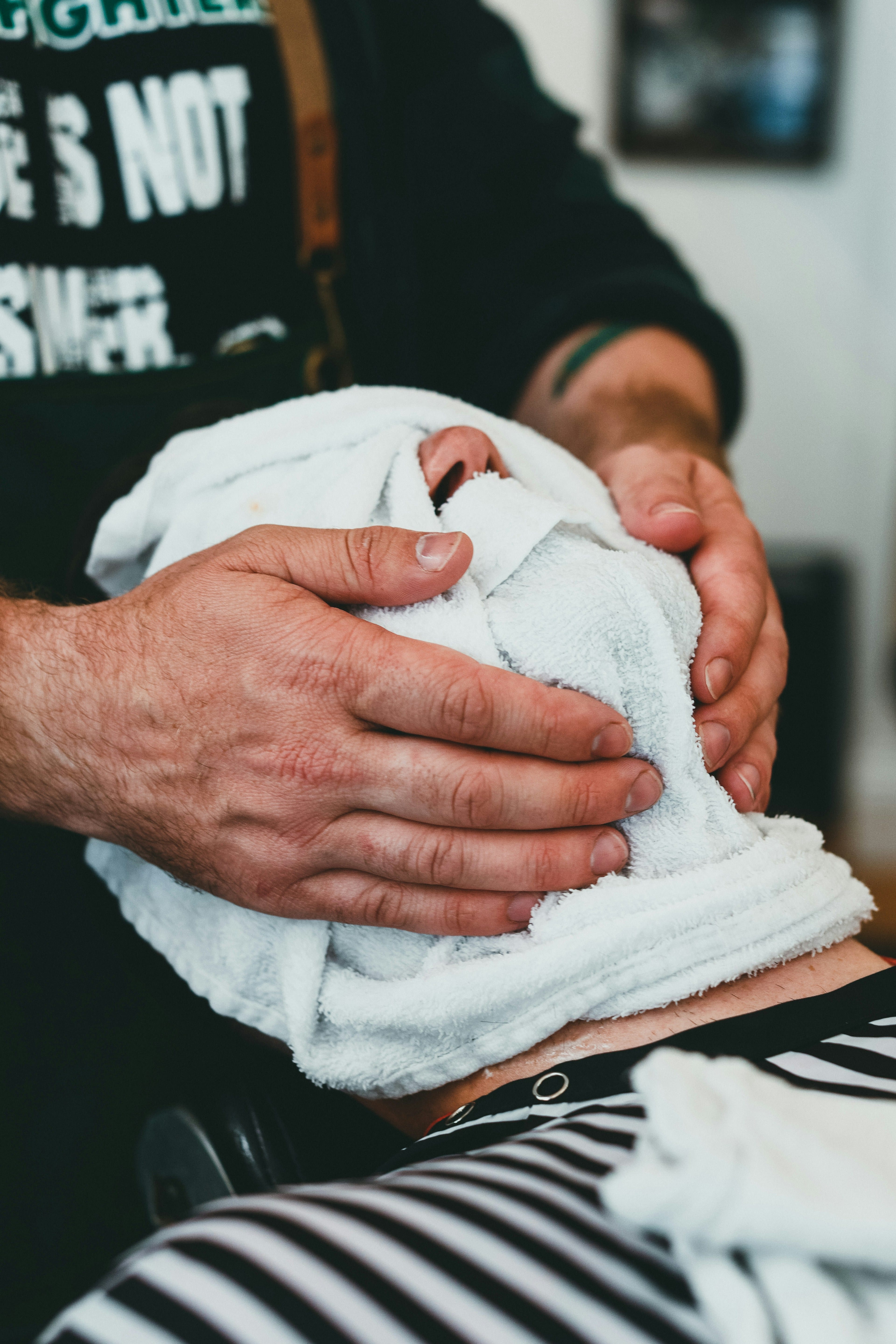 Barber wrapping a client with a hot towel during a grooming service