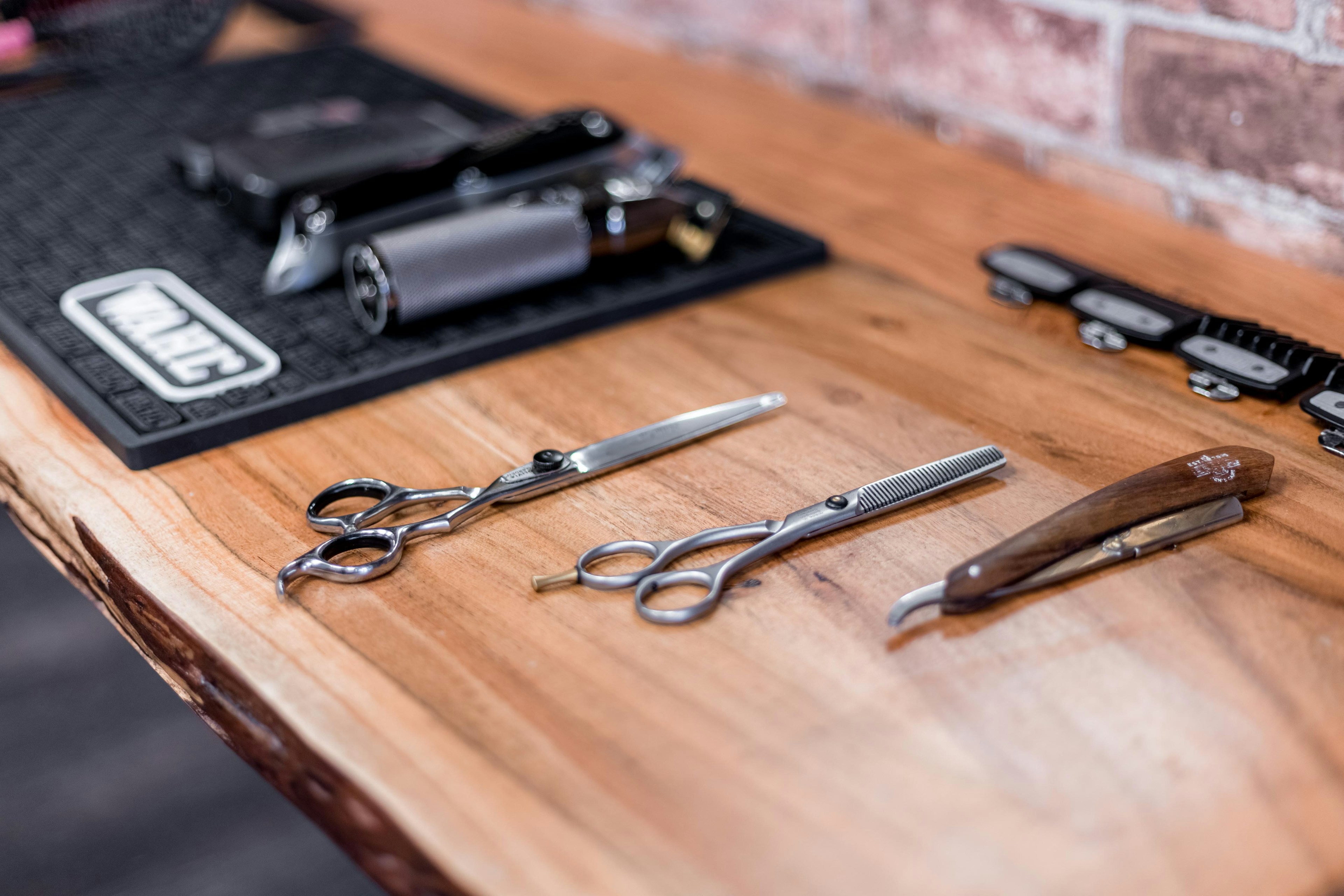 Scissors, straight razor, and clippers laid out on a wooden counter